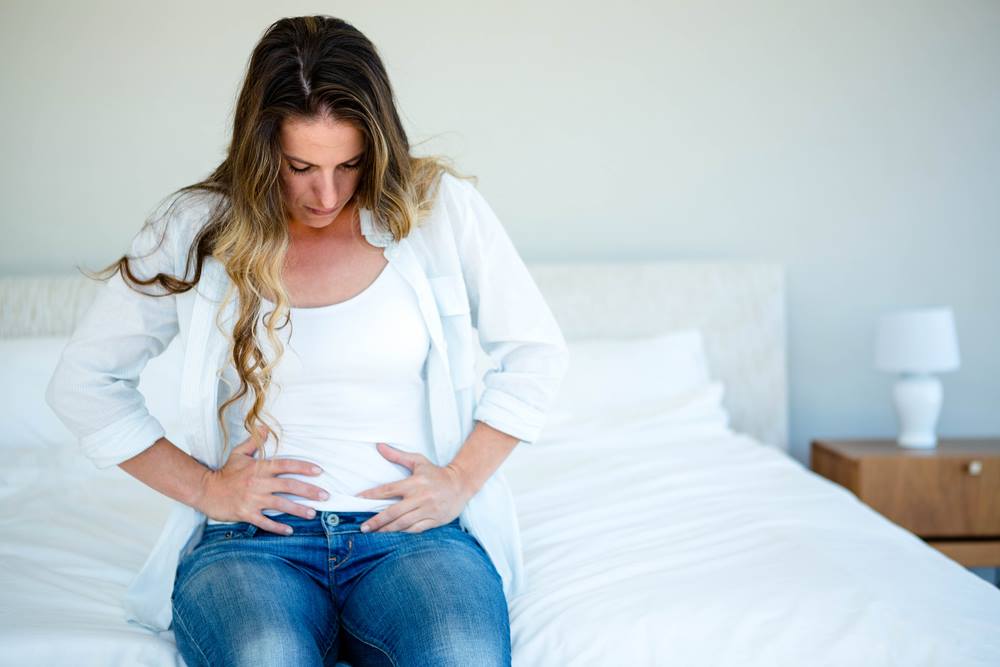 woman sitting on bed holding her stomach concerned about implantation bleeding