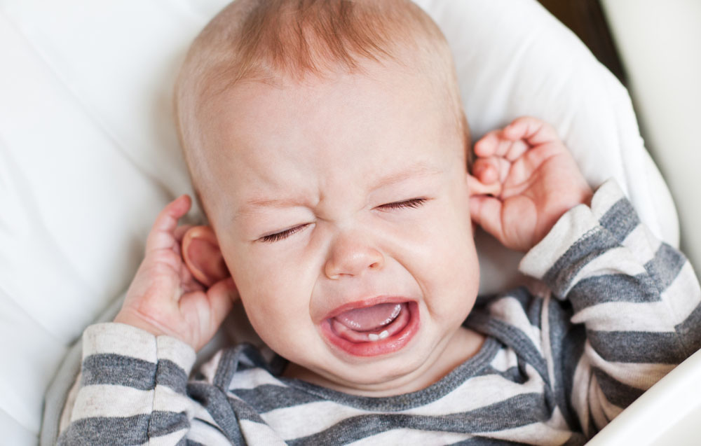 Getting sleep while raising children. Cute little boy crying and holding his ear on a white background