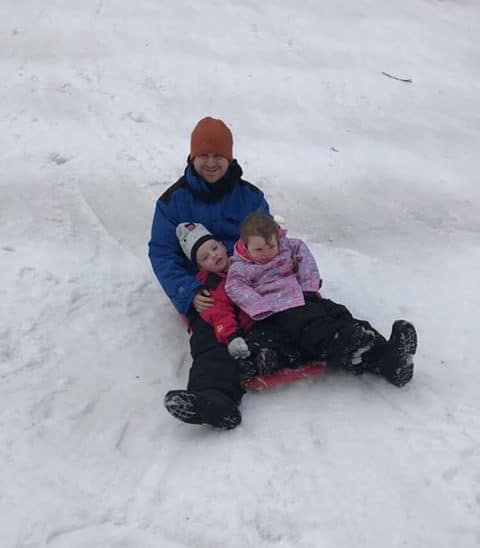 Father and 2 children tobogganing in snow at Corin Forest